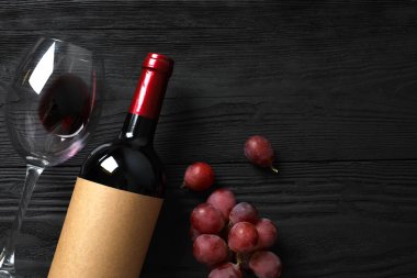 Ahşap zemin üzerinde üzüm ve bardak bulunan bir şişe kırmızı şarap.