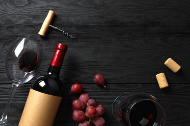 Ahşap zemin üzerinde üzüm ve bardak bulunan bir şişe kırmızı şarap.