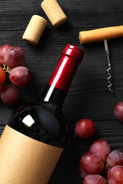 Üzümlü bir şişe kırmızı şarap, ahşap arka planda tirbuşon ve mantar.