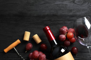 Üzümlü bir şişe kırmızı şarap, ahşap arka planda tirbuşon ve mantar.