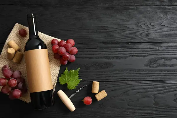 Ahşap arka planda üzüm ve mantarlı bir şişe kırmızı şarap.