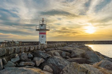 Günbatımında Jetty 'deki kırsal deniz feneri, kayalıklardaki yıpranmış deniz fenerinde gün batımı parlıyor.