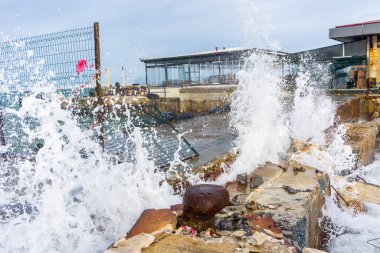 Waves Crashing Against Concrete.  White Waves Breaking on a Rocky Coast. Dramatic Splash of Sea Foam Against Concrete clipart