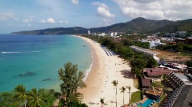 Karon sahiline insansız hava aracı yaklaşımı, kıyı şeridi, altın kum ve turkuaz su, palmiye ağaçları. Phuket 'teki Karon Sahili' nin geniş ve güzel kıyıları, tatilciler, adada hayat, doğa, yeşil ağaçlar ve