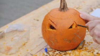Cadılar Bayramı için balkabağı hazırlıyorum. Yetişkin birinin elleri balkabağıyla korkunç bir şekil oyuyor. Cadılar Bayramı dekorasyonu.