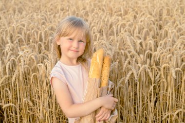 Buğday tarlasında Fransız ekmeği ekmeği tutan mutlu küçük sarışın kız. Ekmekli çocuklar. Buğday hasadı