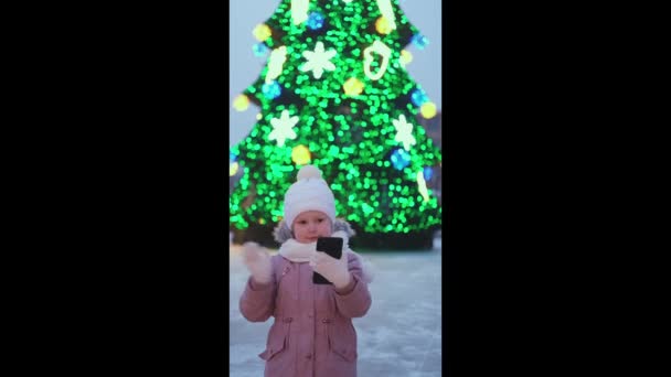 Κοριτσάκι Στέκεται Στο Δρόμο Κοντά Στο Χριστουγεννιάτικο Δέντρο Φώτα Μιλώντας — Αρχείο Βίντεο