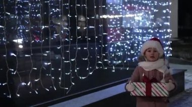 Noel Baba şapkalı mutlu küçük kız kışın açık havada Noel hediyesi veriyor. Noel, çocukluk tatili konseptini sunar