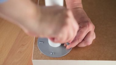 Bir kadın işçi bağlayıcıyı masanın bacağına tornavidayla çeviriyor. Mobilya kurulumu.