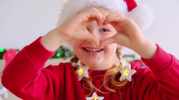 Feliz Niña Gorra Navidad Hacer Dedo Corazón Mirar Cámara Felicitar — Vídeo de stock