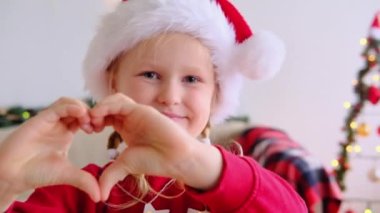 Xmas şapkalı mutlu küçük kız kameraya bakıp Noel tatili için çocukları kutluyor. Mutlu küçük çocuklar yeni yıl video tebrik kartı çekerler. Kapatın. video günlüğü yazarı