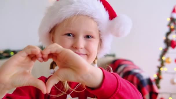 Feliz Niña Gorra Navidad Hacer Dedo Corazón Mirar Cámara Felicitar — Vídeos de Stock