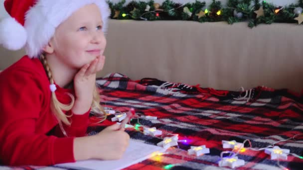 Счастливая Маленькая Девочка Шляпе Санта Клауса Лежит Дома Кровати Пишет — стоковое видео