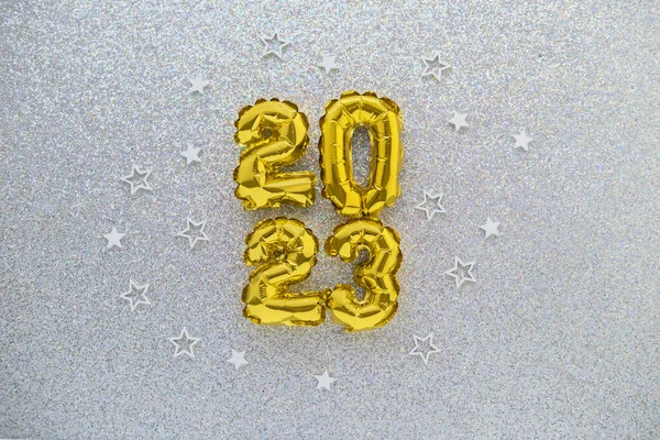2023 gold foil balloons and confetti on silver glitter background. Festive concept.
