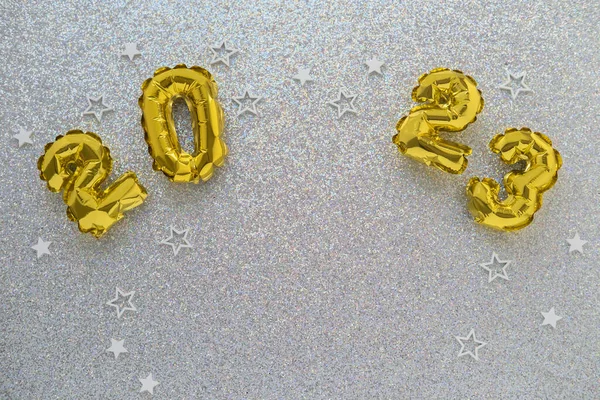 2023 gold foil balloons and confetti on silver glitter background. Festive concept.