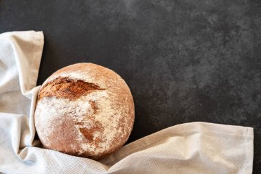 Freshly baked bread loaves with kitchen towel on black background. Top view. Copy space