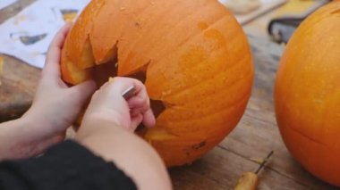 Cadılar Bayramı için balkabağı hazırlıyorum. Yetişkin birinin elleri balkabağıyla korkunç bir şekil oyuyor. Cadılar Bayramı dekorasyonu.