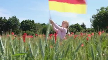 A little blond girl with a Germany flag on her hands on a green wheat field with poppies in summer. Flag of Germany. patriotism, independence day