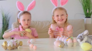 Tavşan kulaklı kız kardeşler çikolata yumurtası avlar onları yer ve evdeki masada kutlama yaparlar. Çocuklar Paskalyayı kutluyor. Paskalya yumurtası avındaki çocuklar.