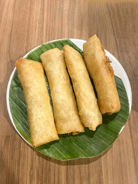 Fried spring rolls on white plate and banana leaves, top view