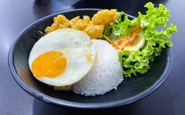Siyah kasede salata ile servis edilen tuzlanmış dory balığı ve yumurtalı pirinç kasesi.