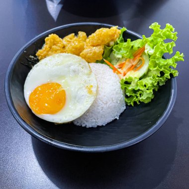 Siyah kasede salata ile servis edilen tuzlanmış dory balığı ve yumurtalı pirinç kasesi.