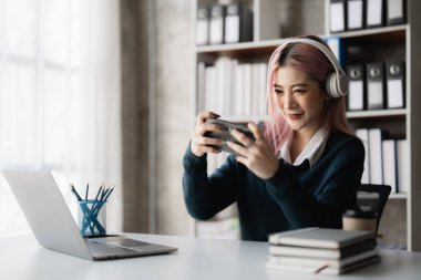 Kulaklık takan heyecanlı Asyalı genç kadın akıllı telefonuyla oynuyor. İnternetli oyuncu.