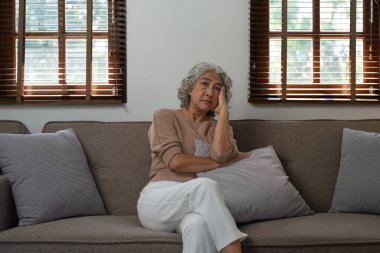 Evdeki kanepede oturan endişeli yaşlı kadının portresi..