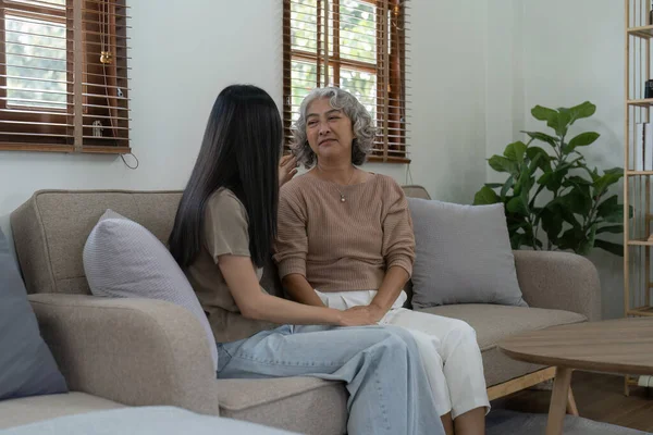 stock image Loving adult daughter hugging older mother on couch at home, family enjoying tender moment together, young woman and mature mum or grandmother looking at each other, two generations.