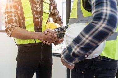 Mimar ve mühendis inşaat işçileri ofis inşaatındaki bir anlaşmayı bitirdikten sonra el sıkışıyorlar, başarı işbirliği konsepti.