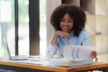 Ofiste dizüstü bilgisayarla çalışan genç Afrikalı Amerikalı iş kadını, ekran laptopuna odaklan, internetten ilginç makaleler oku ve finanse et..
