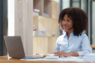 Ofiste dizüstü bilgisayarla çalışan genç Afrikalı Amerikalı iş kadını, ekran laptopuna odaklan, internetten ilginç makaleler oku ve finanse et..