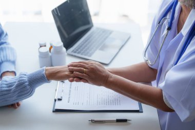 Semptomu açıklarken hastayla sohbet eden ve cesaretlendirmek için el ele tutuşan doktor..