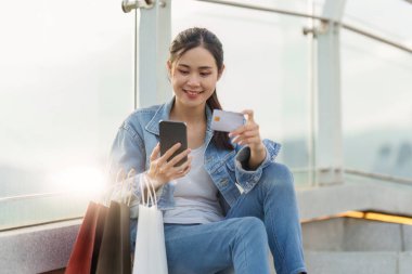 Asyalı modaya uygun bir kadın alışveriş merkezinde alışveriş çantalarıyla yürürken satış promosyonu yapıyor..