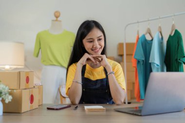 Asyalı Kadın moda tasarımcısı yeni koleksiyon için çalışan yaratıcı terzi. Mutlu çevrimiçi mağaza sahibi nakliye siparişi hazırlıyor.