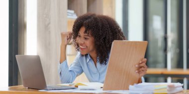 Dizüstü bilgisayarda çalışan siyahi iş kadını mutlu bir şekilde kazanıyor. Heyecanlı kadın zaferi işten iyi haberler alıyor..