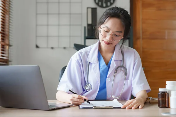 Portrait of female Asian doctor working with patient document in her office at clinic.