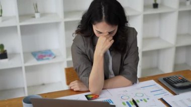 Asya 'lı Kadın masadaki mali dökümanlarla dizüstü bilgisayar kullanırken stresli görünüyor. Kadın evde çalışıyor. Yüksek kalite 4k görüntü