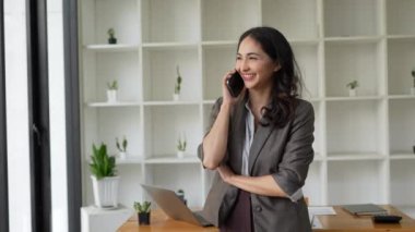 İş kadını ofiste müşteriyle telefon görüşmesi yapıyor. Akıllı telefon kullanan Asyalı genç bir kadın..