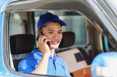 Paket ve teslimat konsepti olan Asyalı kurye. Teslimatçı müşteriyle telefonla konuşuyor..
