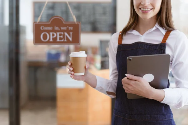 Young Female manager in restaurant with tablet. Woman coffee shop owner with open sign. Small business concept.