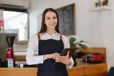 Young Female manager in restaurant with tablet. Woman coffee shop owner with open sign. Small business concept.