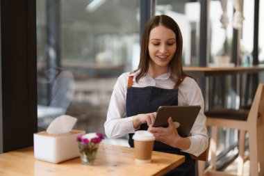 Young Female manager in restaurant with tablet. Woman coffee shop owner with open sign. Small business concept.