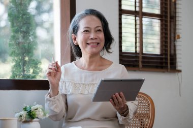Smart asian mature middle-aged businesswoman CEO boss leader teacher using tablet, e-learning, working remotely online in home office.