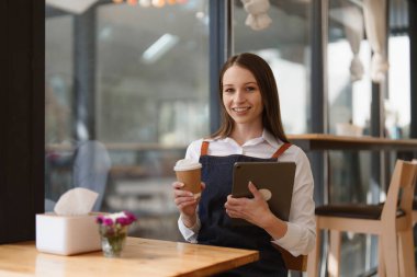 Young Female manager in restaurant with tablet. Woman coffee shop owner with open sign. Small business concept.
