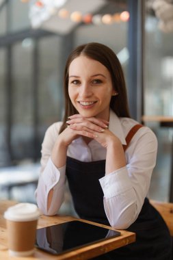Young Female manager in restaurant with tablet. Woman coffee shop owner with open sign. Small business concept.