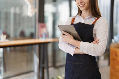Young Female manager in restaurant with tablet. Woman coffee shop owner with open sign. Small business concept.