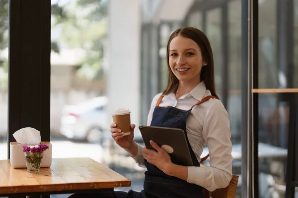 Young Female manager in restaurant with tablet. Woman coffee shop owner with open sign. Small business concept.