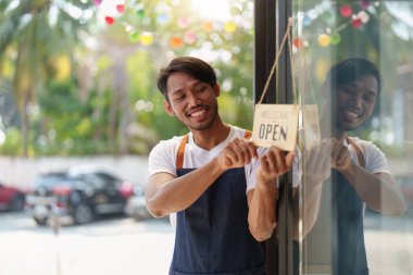 Young male manager in restaurant with tablet. Man coffee shop owner with open sign. Small business concept.