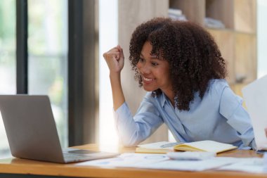 Dizüstü bilgisayarda çalışan siyahi iş kadını mutlu bir şekilde kazanıyor. Heyecanlı kadın zaferi işten iyi haberler alıyor..